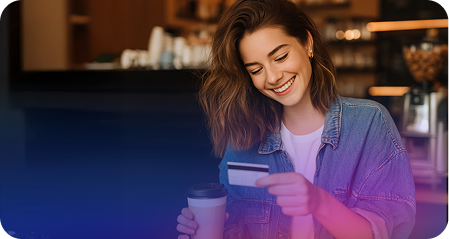 Lady smiling while holding a coffee in one and a credit card on the other hand